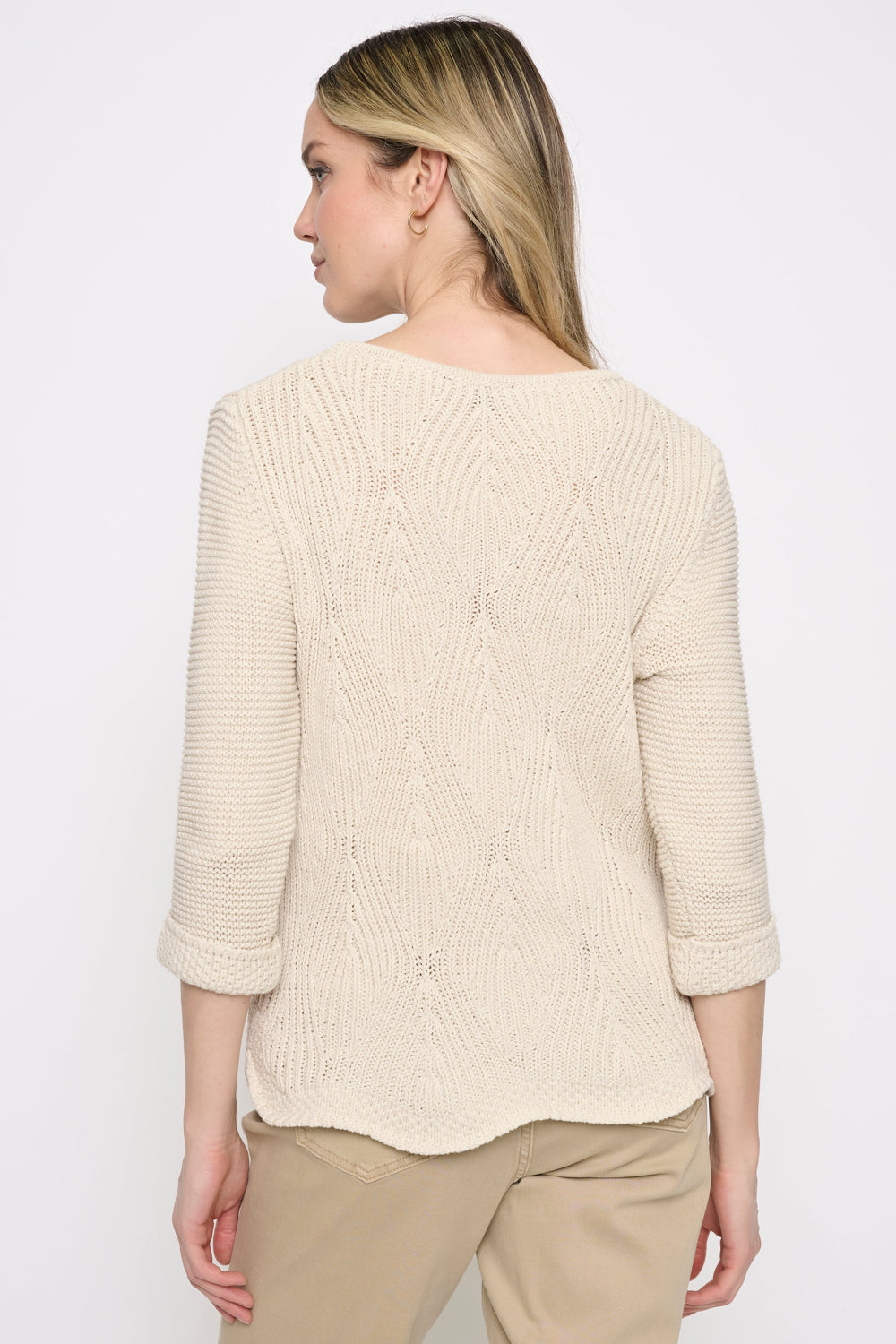 A woman shown from the back wearing a cream-colored, three-quarter sleeve cable-knit sweater and beige pants against a plain white studio background.