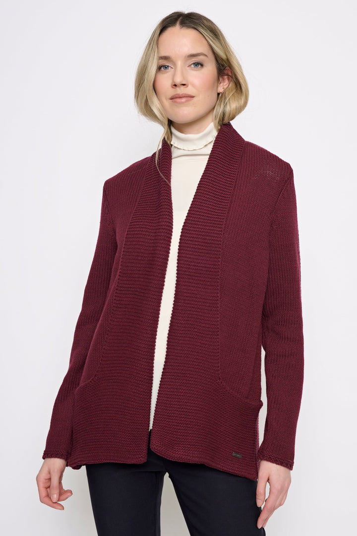 A woman modeling a ribbed open-front cardigan in deep burgundy, worn over a cream turtleneck and black pants, against a plain light gray studio background.