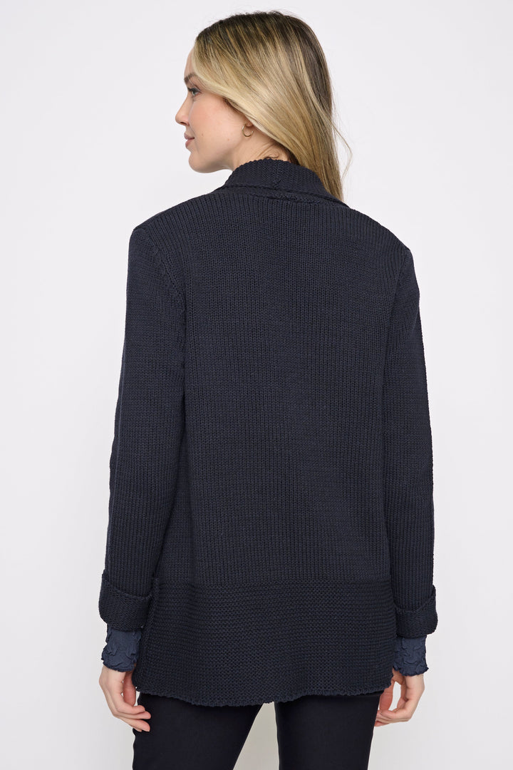 A woman shown from the back wearing a dark navy ribbed knit cardigan or sweater jacket over a matching dark top and black pants, against a plain white studio background.
