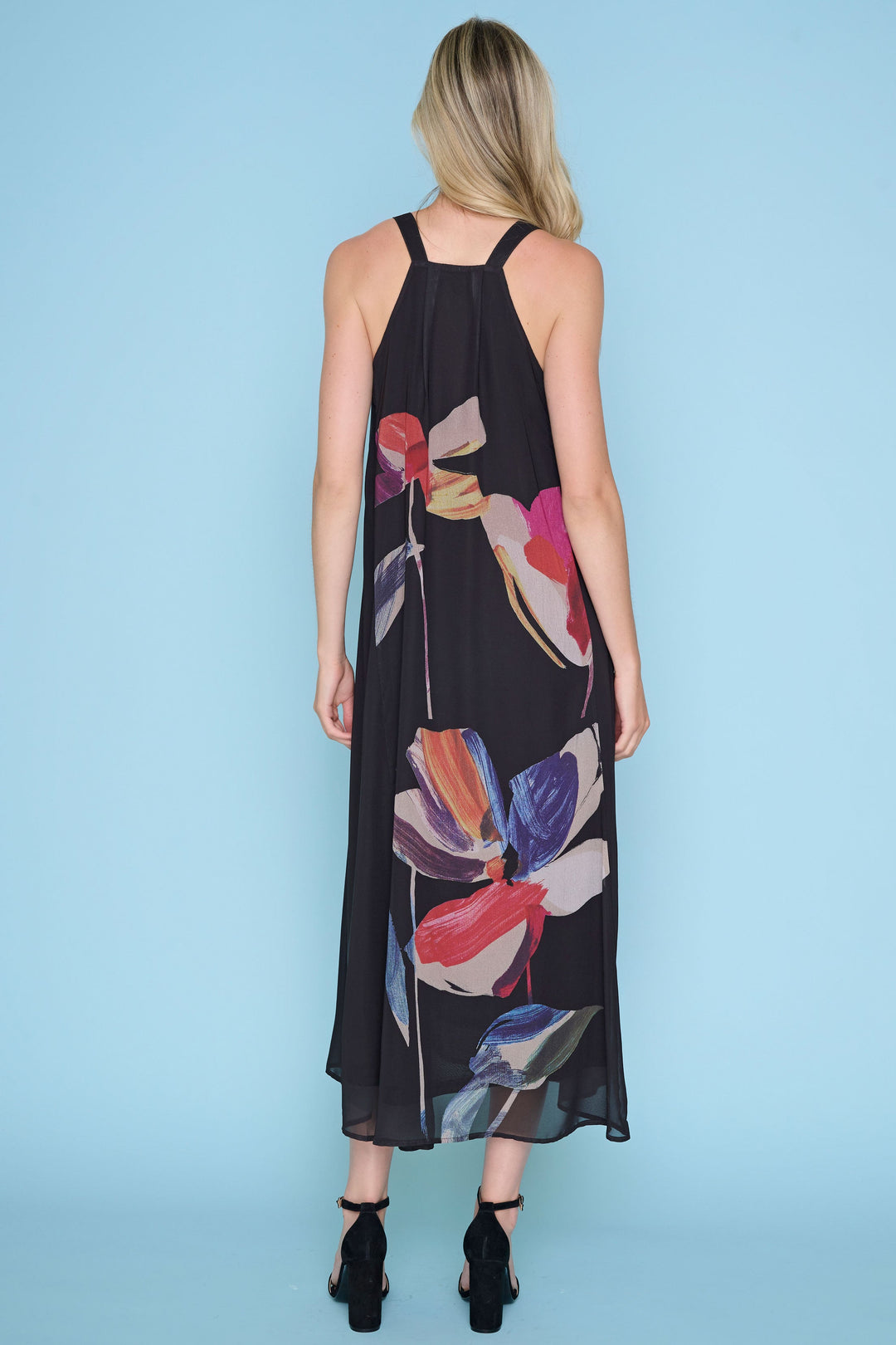 Woman wearing a black sleeveless dress with colorful floral patterns on a light blue background