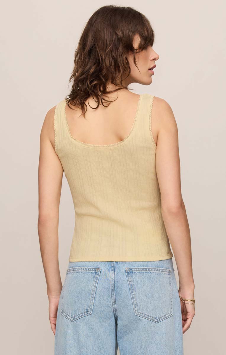 Woman wearing a light yellow tank top and blue jeans against a neutral background