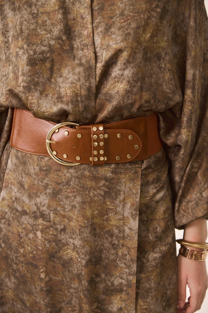Close-up of a person wearing a brown leather belt with gold buckle and studded details.