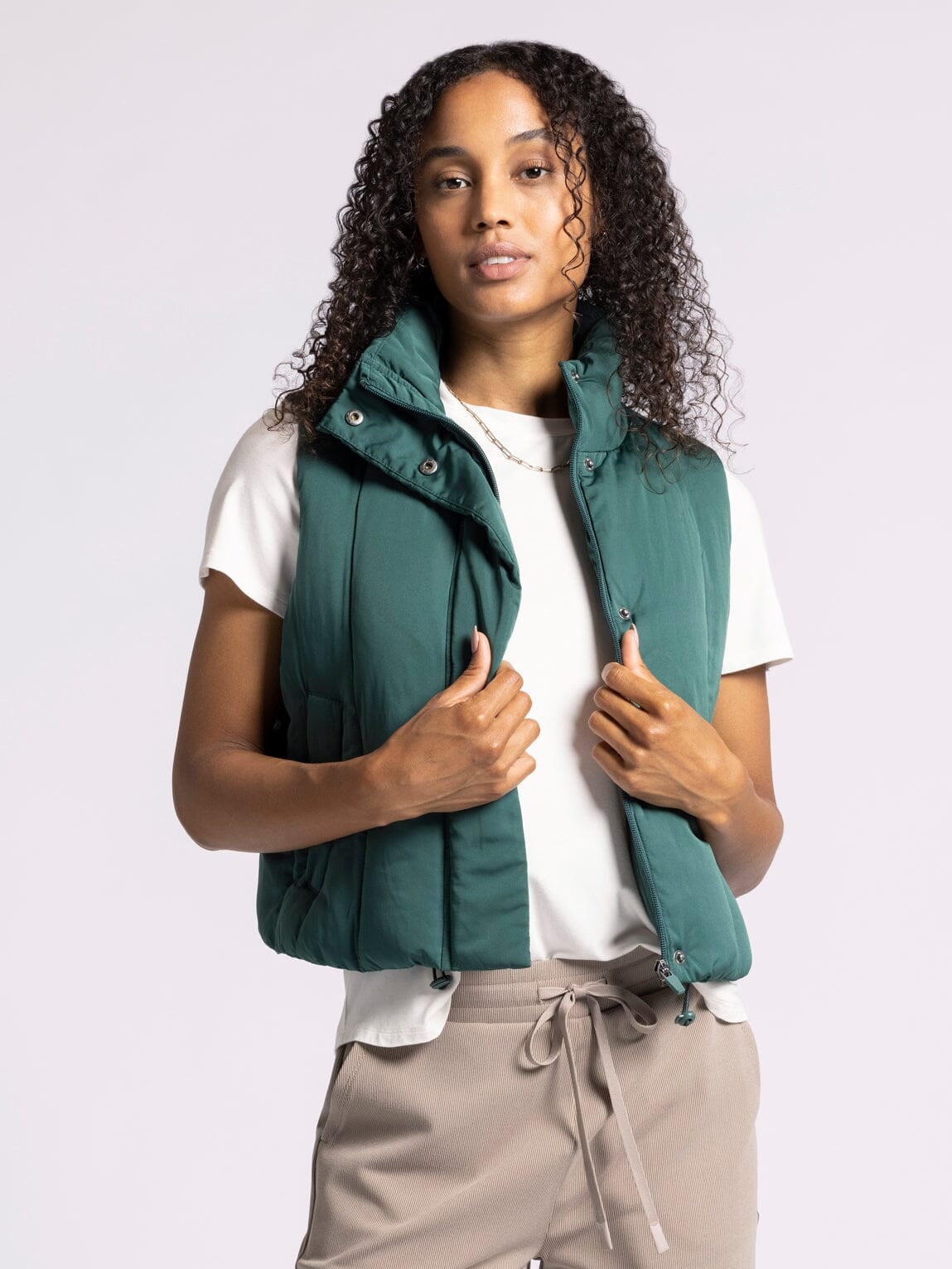 Person wearing a green puffer vest over a white shirt on a light gray background