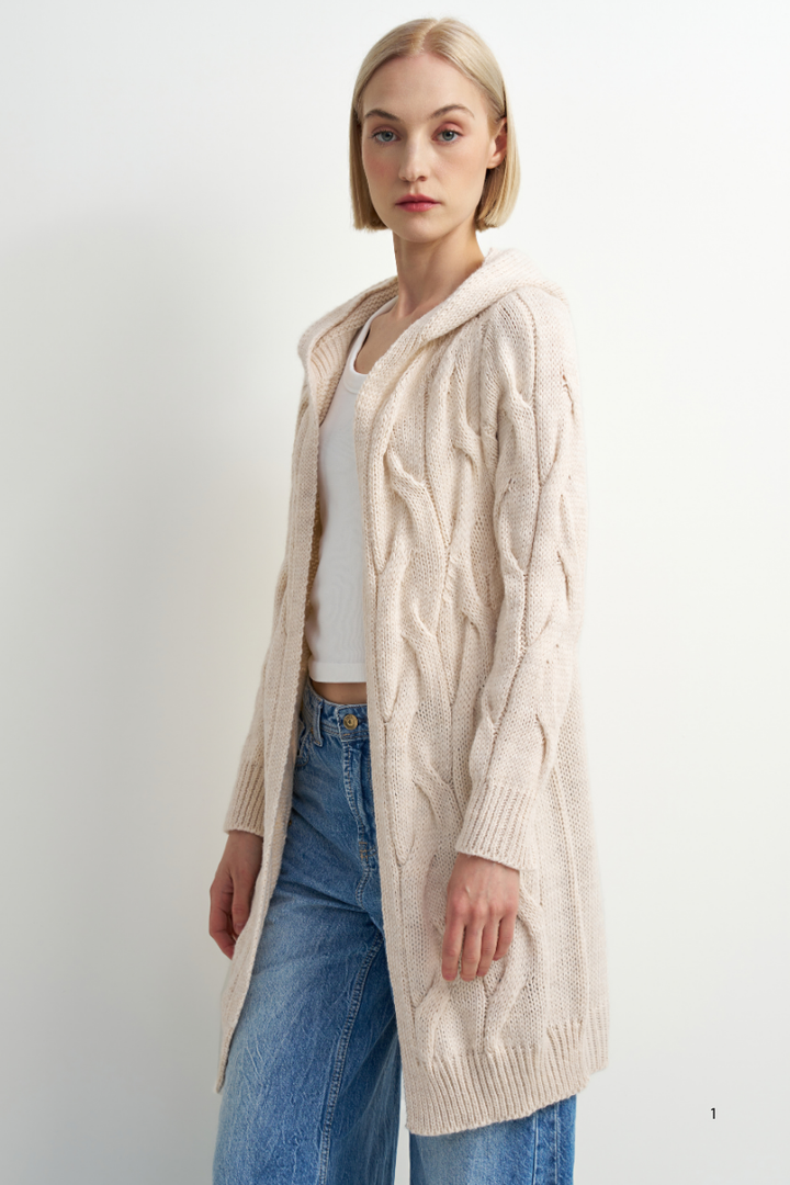 A woman modeling a long cream cable-knit hooded cardigan over a white top and blue jeans, standing against a plain white studio background.