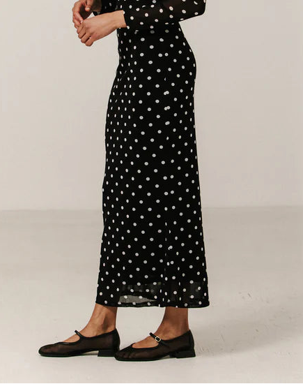 Woman wearing a black dress with white polka dots against a plain background