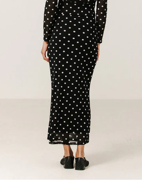 Woman wearing a black dress with white polka dots on a plain background