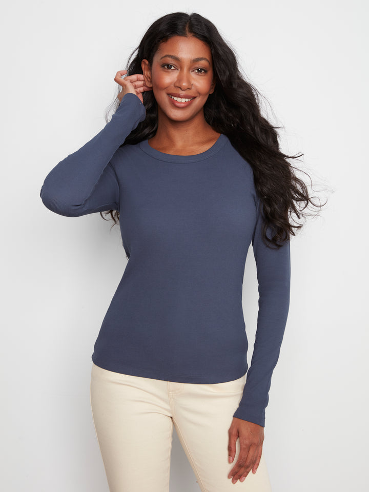 Woman wearing a blue long-sleeve top and beige pants against a white background