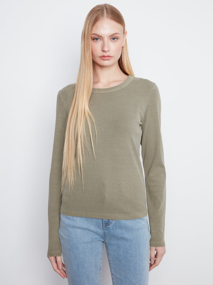 A blonde model wearing a long-sleeve crewneck knit sweater in olive green, paired with light blue jeans, against a plain light gray studio background.