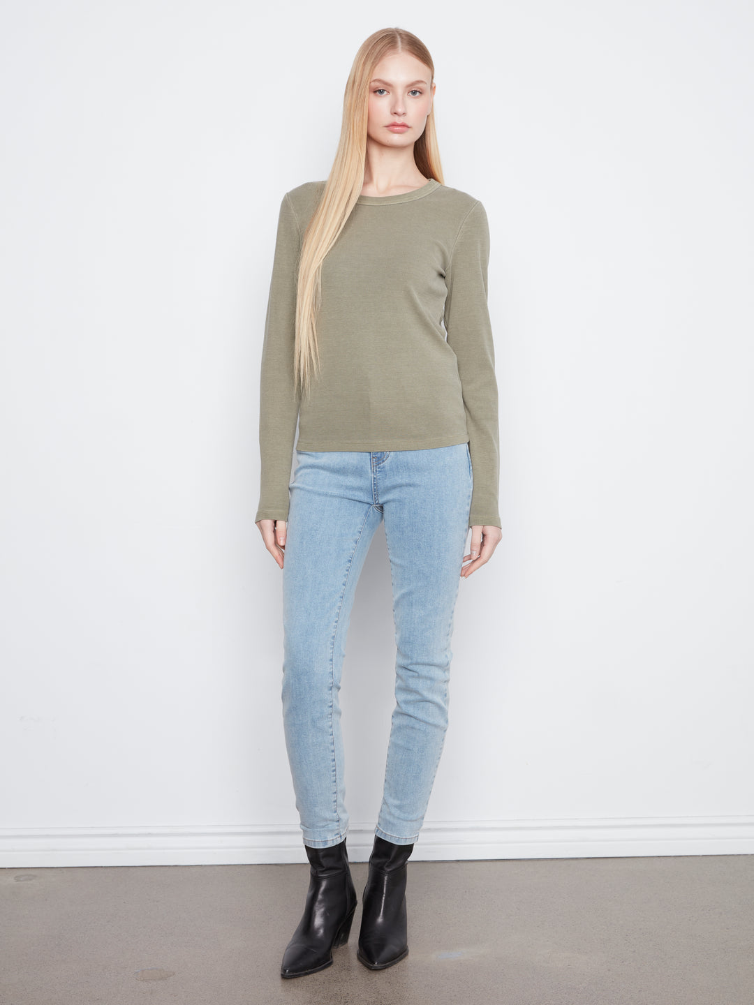 Woman wearing a green sweater and light blue jeans against a white background