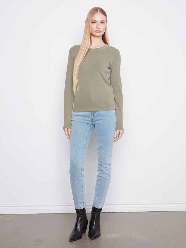 Woman wearing a green sweater and light blue jeans against a white background
