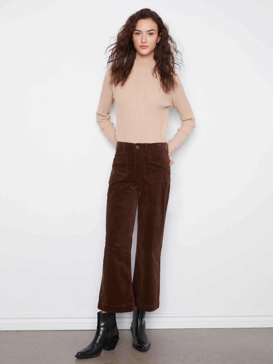Woman wearing a beige sweater and brown corduroy pants against a white background