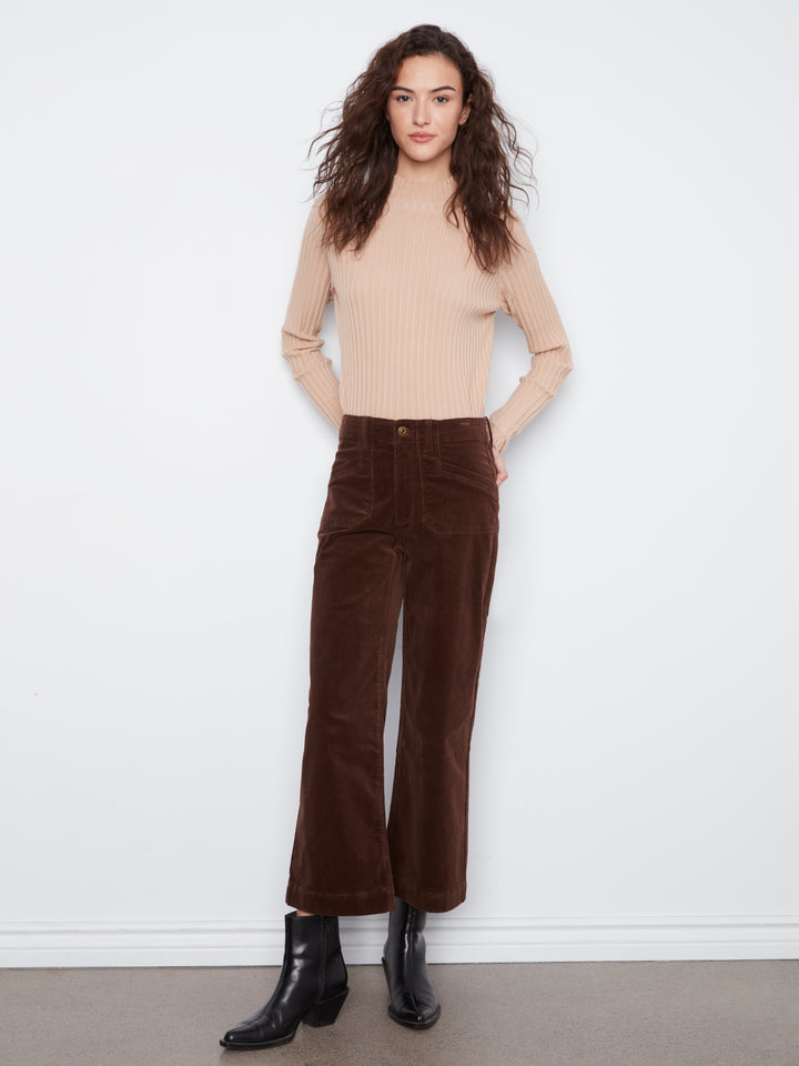Woman wearing a beige sweater and brown corduroy pants against a white background