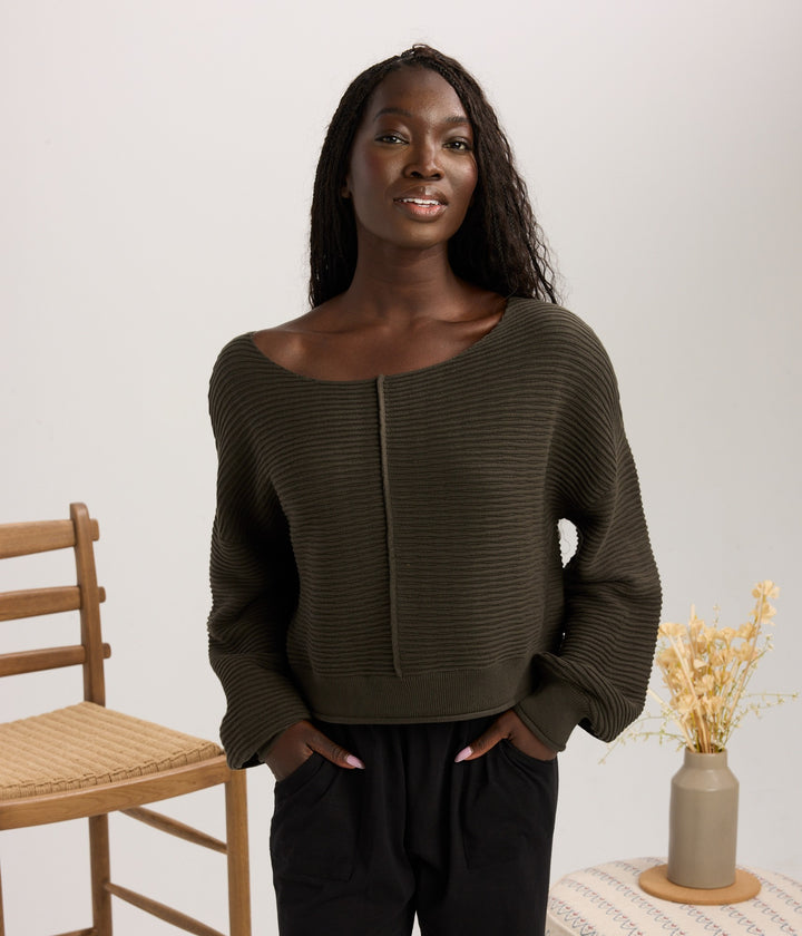 A woman modeling a dark olive green ribbed knit sweater with a wide boat neckline.