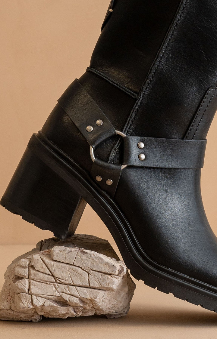 Black leather boot with a strap and buckle on a beige background