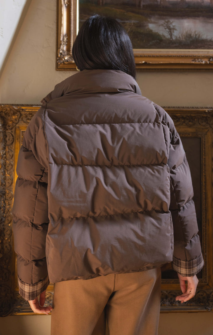 Person wearing a brown puffer jacket standing in front of ornate wall art.