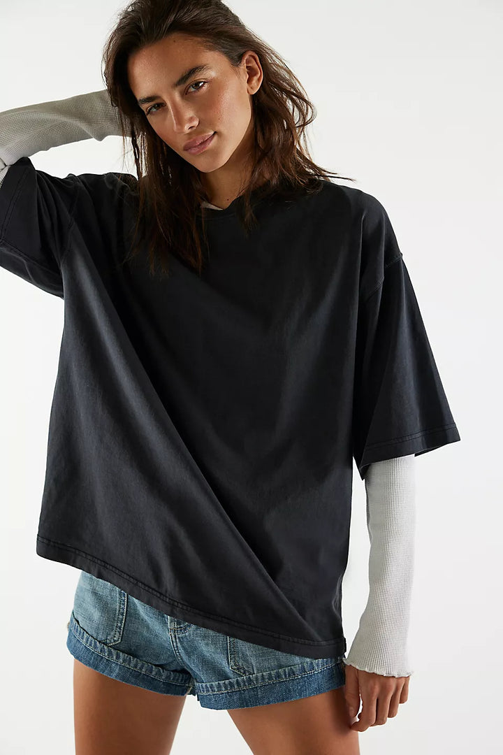 Woman wearing a black oversized shirt with a white long-sleeve shirt underneath on a white background