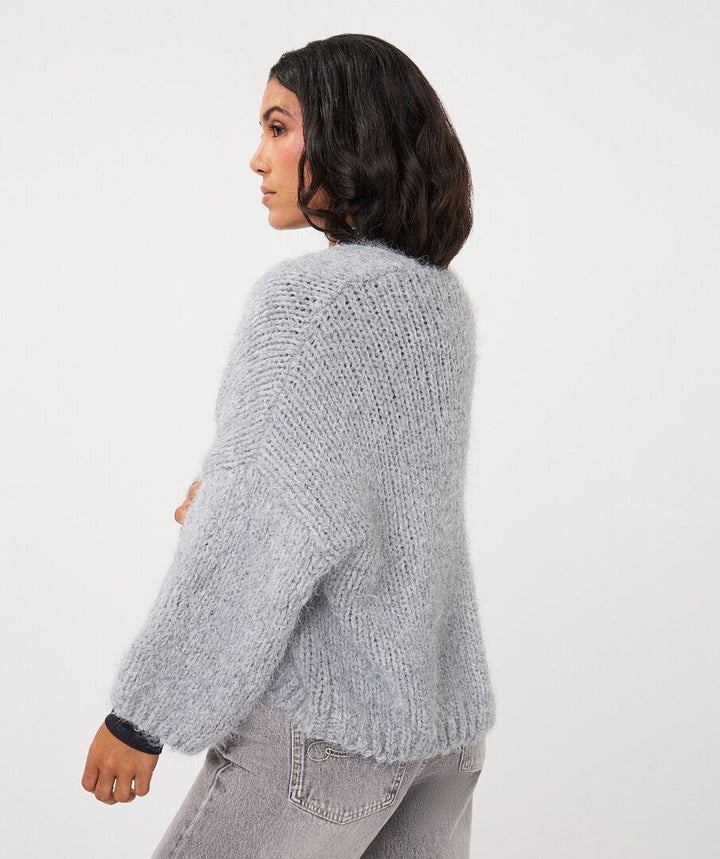 A woman shown from the back wearing a light gray chunky knit cardigan sweater and gray jeans, photographed against a plain white studio background.