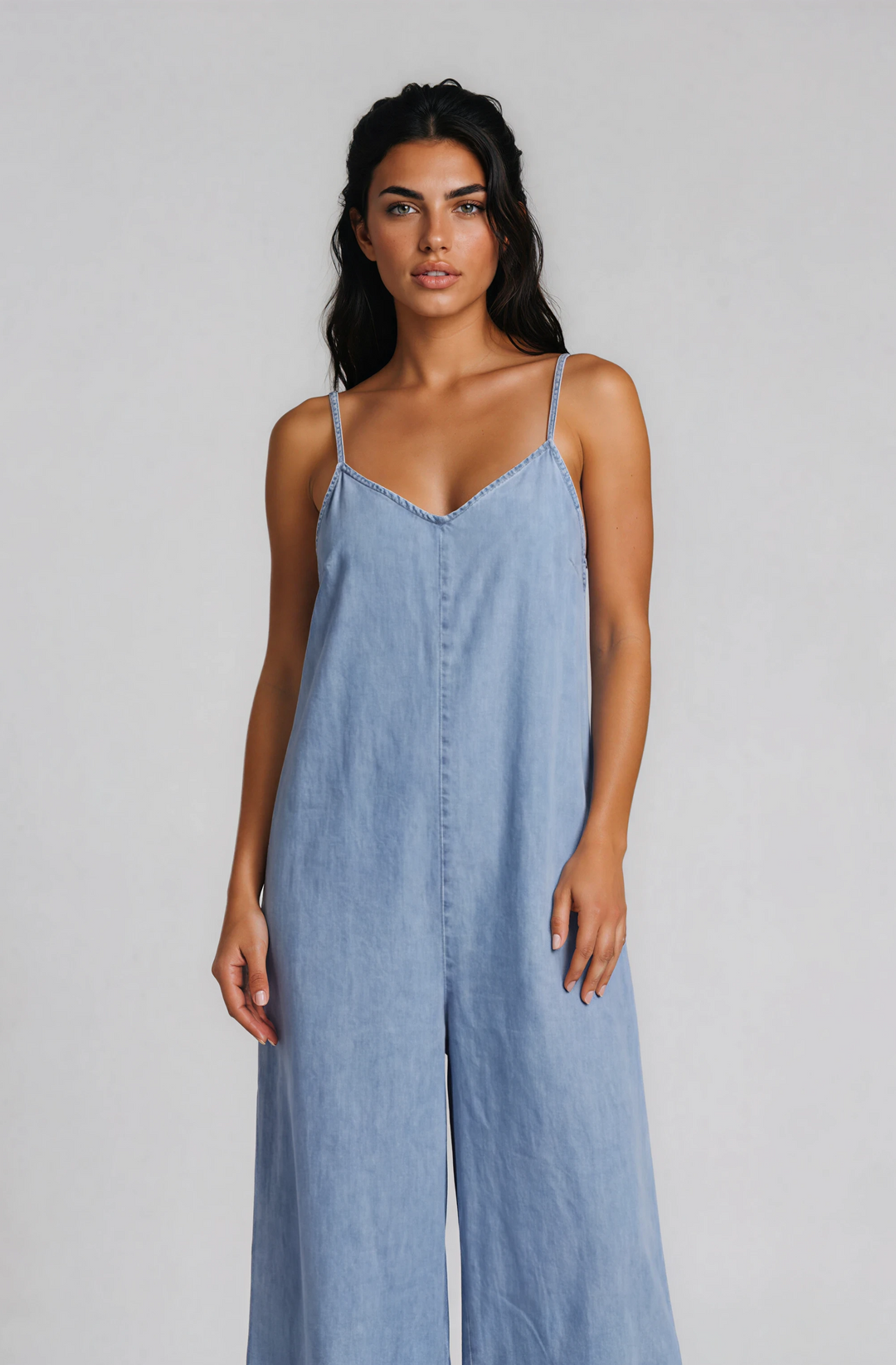 Woman wearing a light blue denim jumpsuit on a plain background