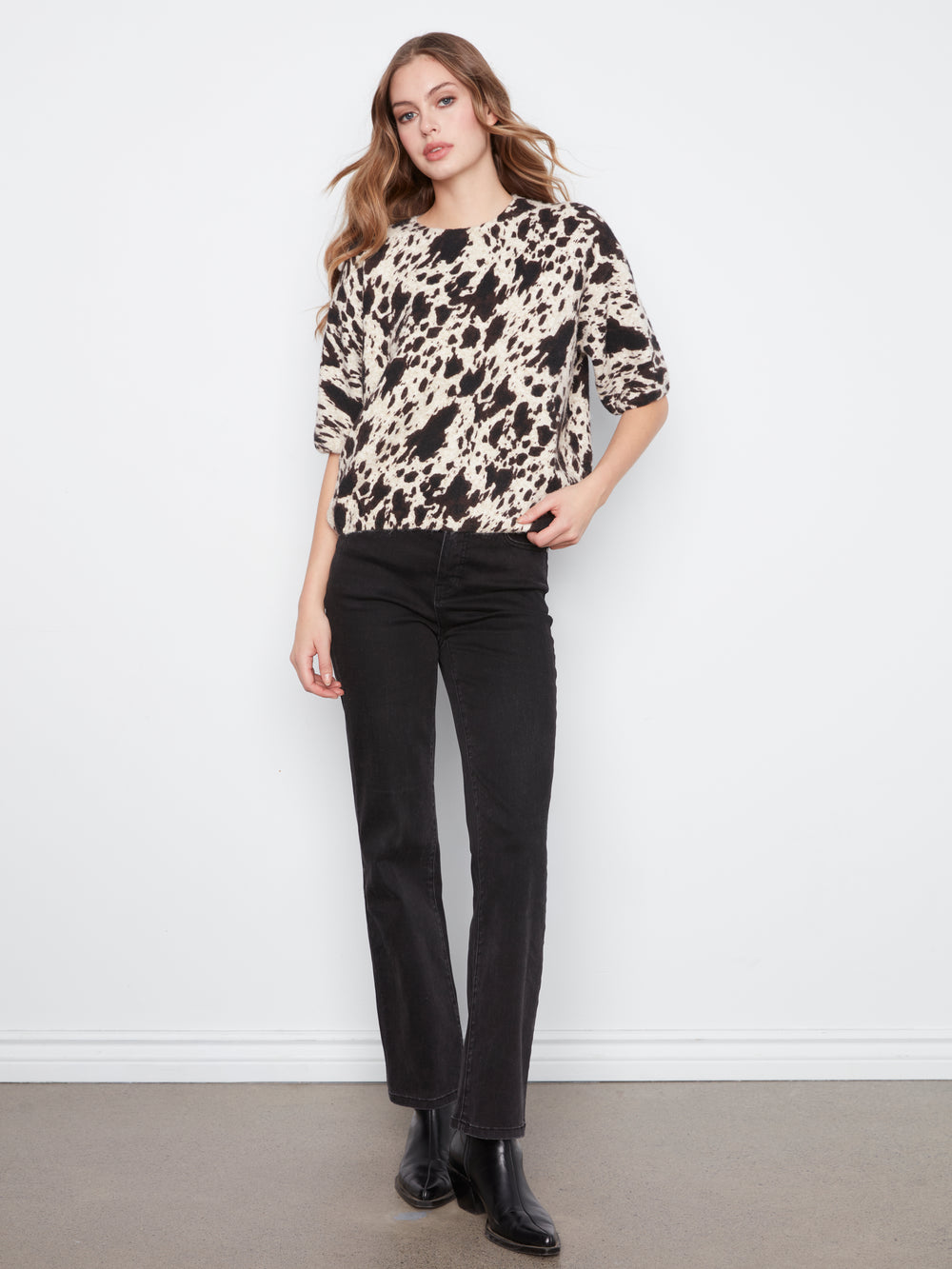 Woman wearing a patterned sweater and black pants against a white background