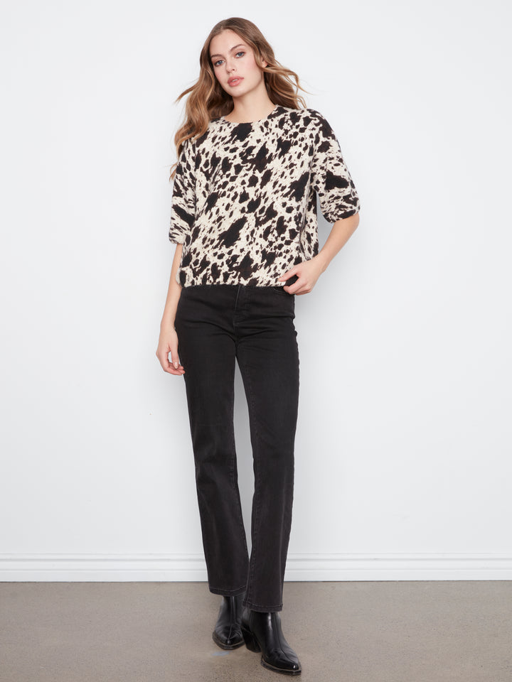 Woman wearing a patterned sweater and black pants against a white background