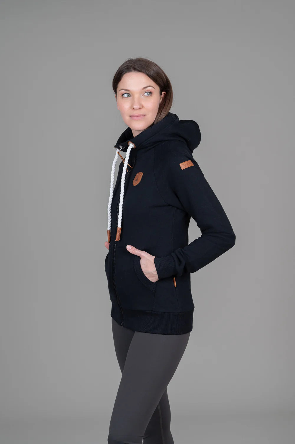 Woman wearing a black hoodie with brown accents on a gray background