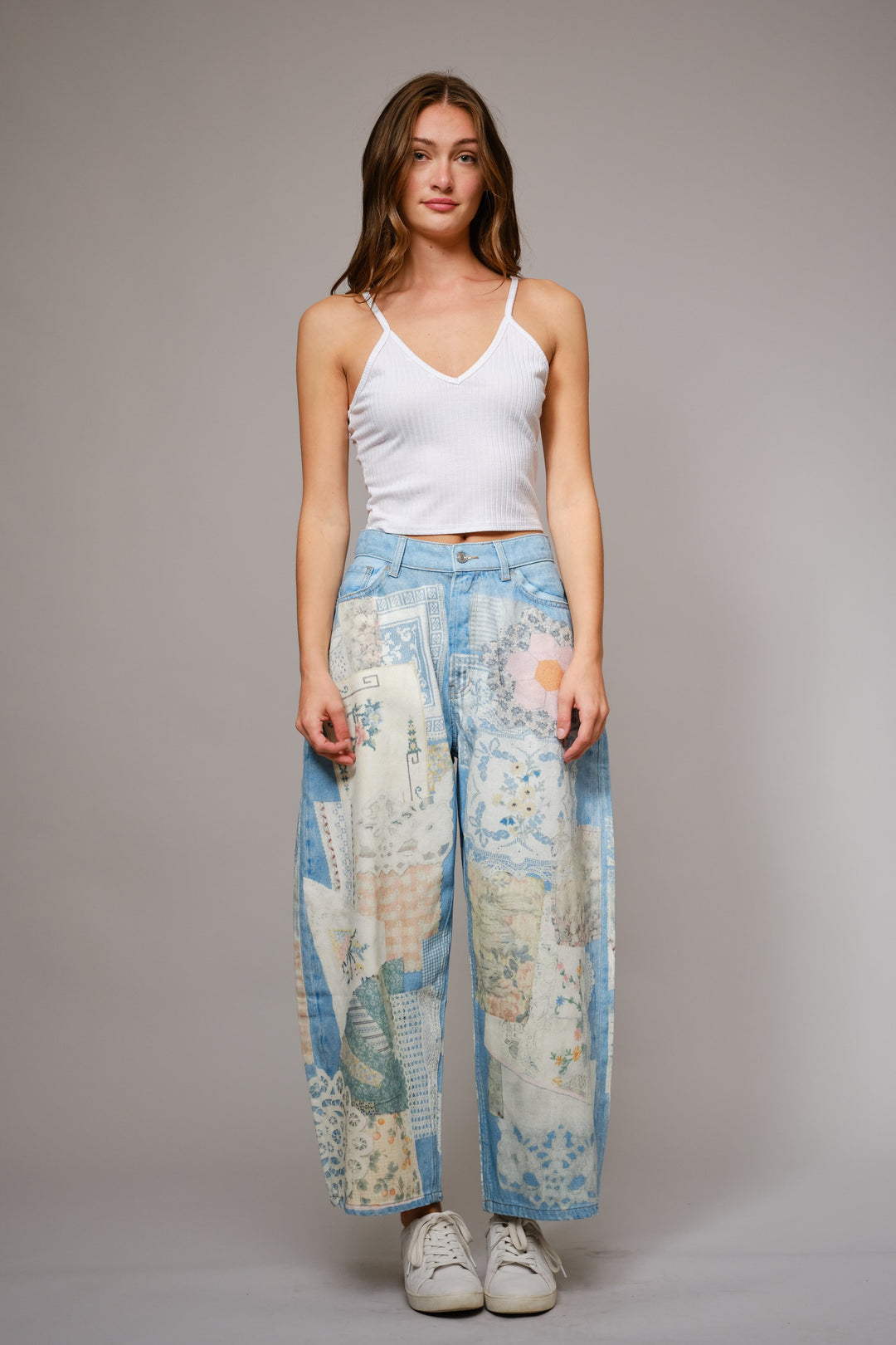 Woman wearing a white tank top and map-patterned pants on a plain background