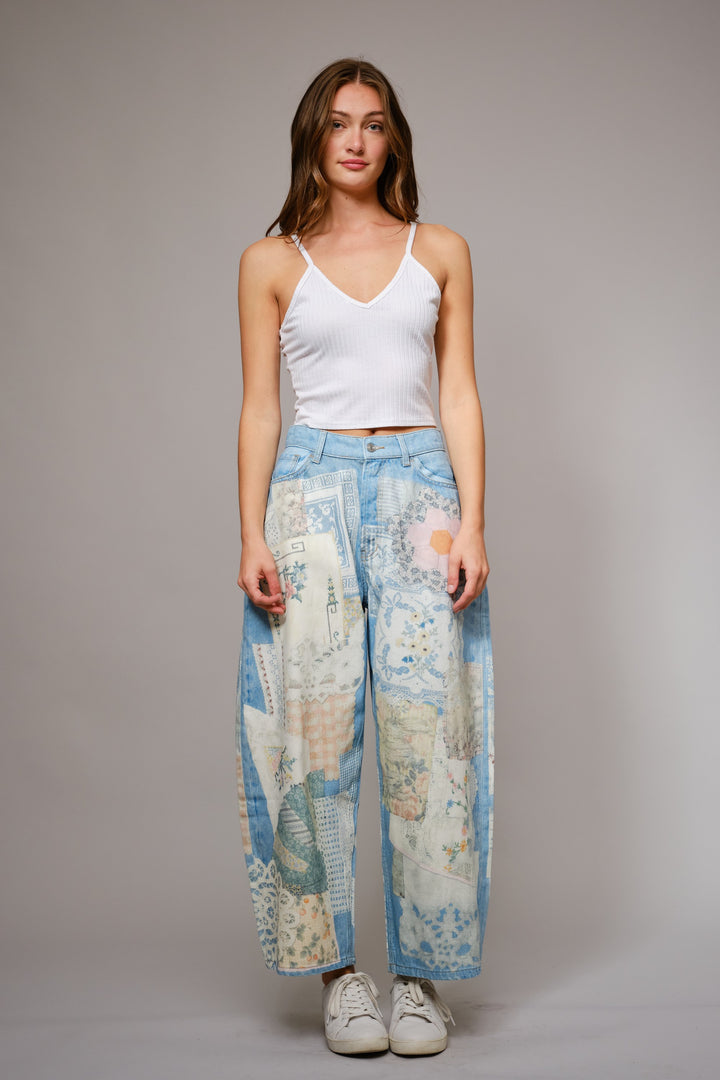 Woman wearing a white tank top and map-patterned pants on a plain background