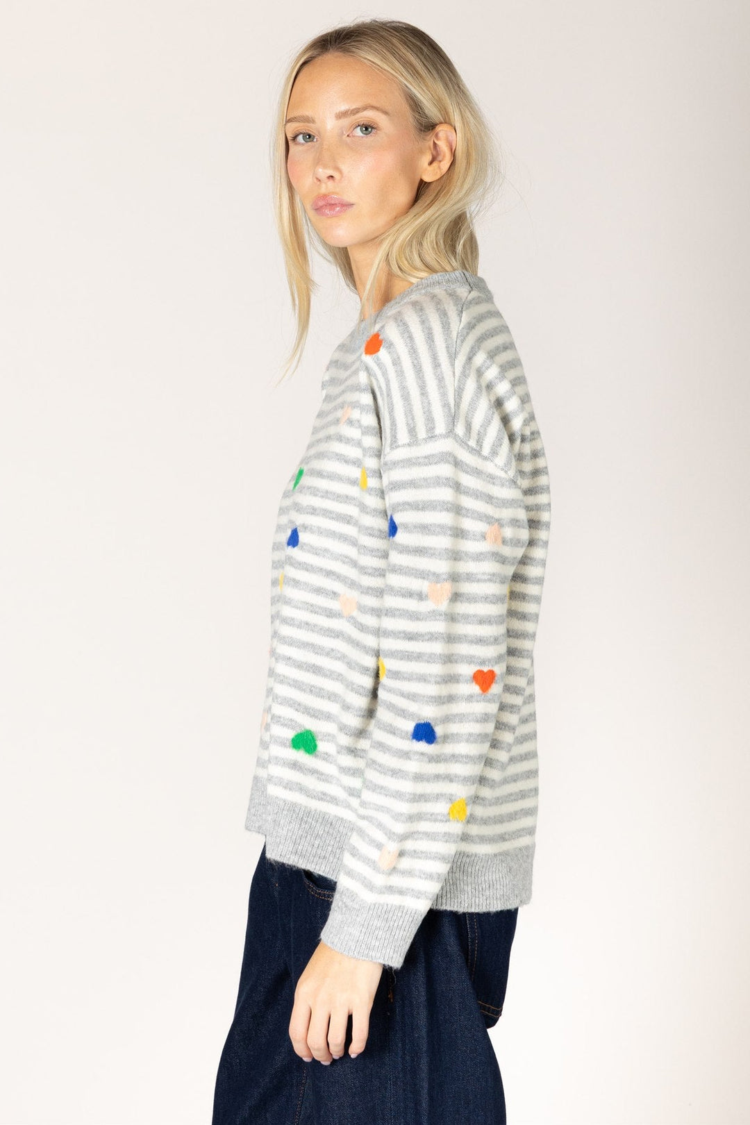 Woman wearing a striped sweater with colorful heart patterns on a plain background