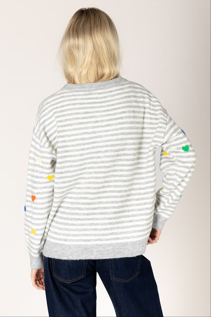 Person wearing a striped sweater with colorful heart patterns on a plain background