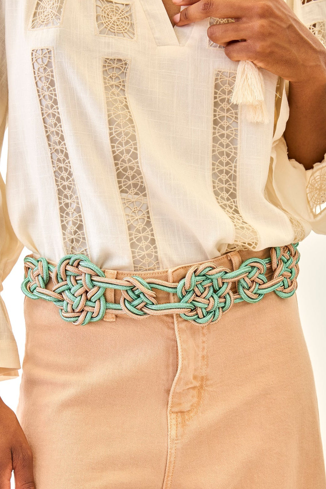 Person wearing a white blouse with lace details and beige pants with a green braided belt.