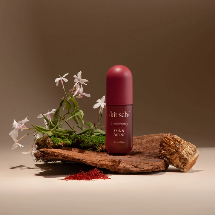 Kit-sch bottle of Oak &amp; Amber on a wooden platform with flowers and natural elements.