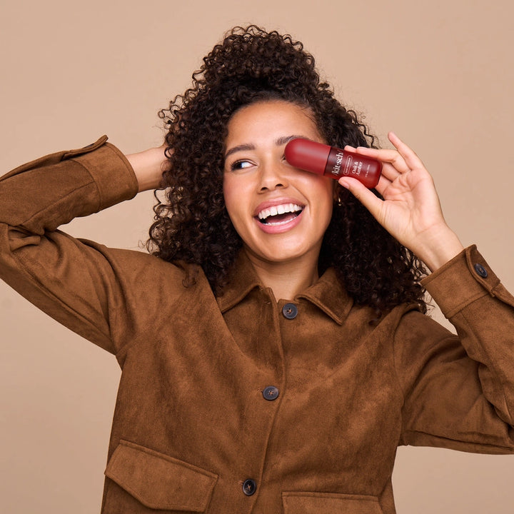 Woman holding a red lipstick against her face on a beige background