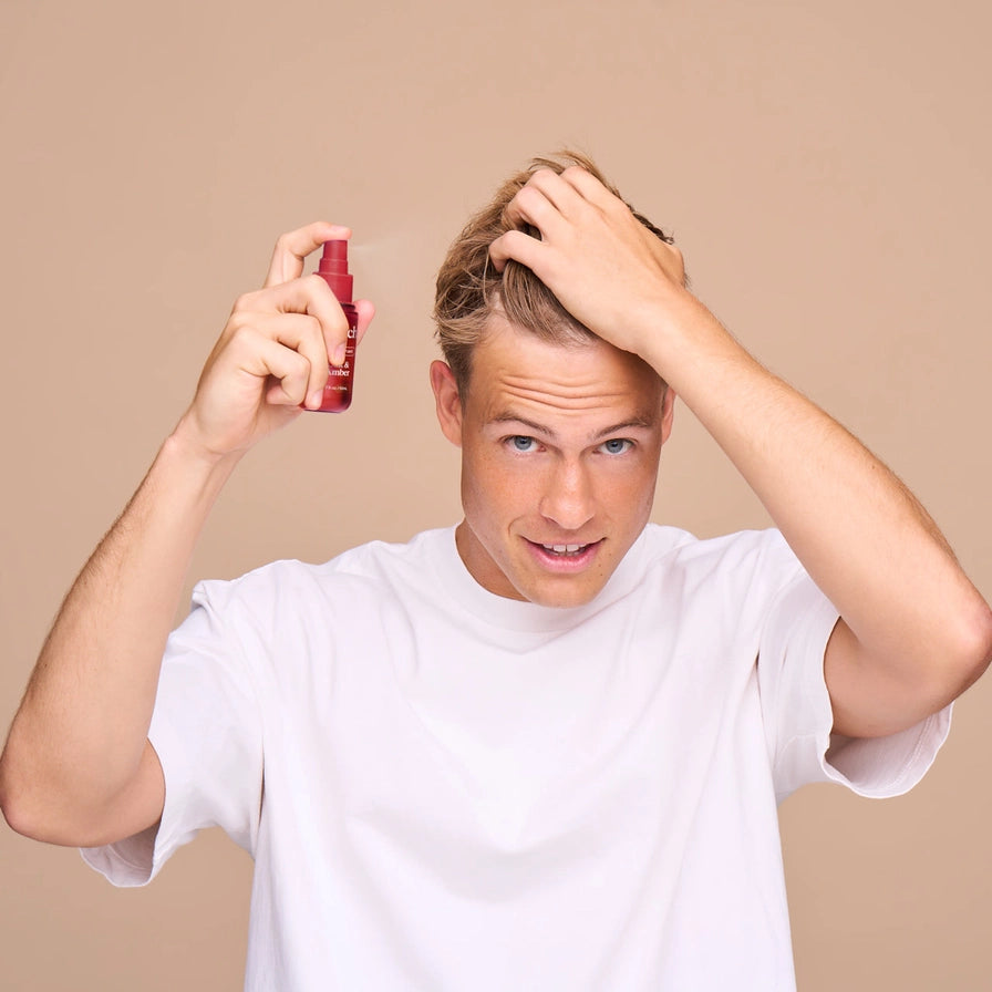 Man applying hair product with a spray bottle on a beige background