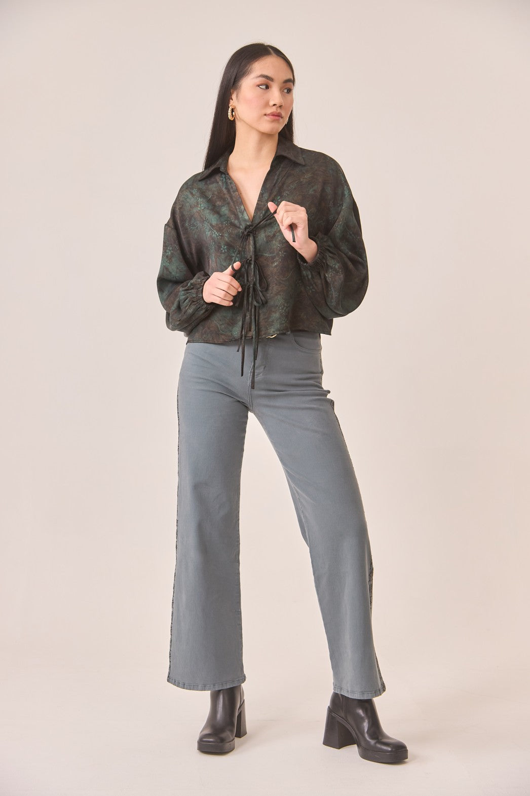 Woman wearing a patterned shirt and gray pants against a plain background