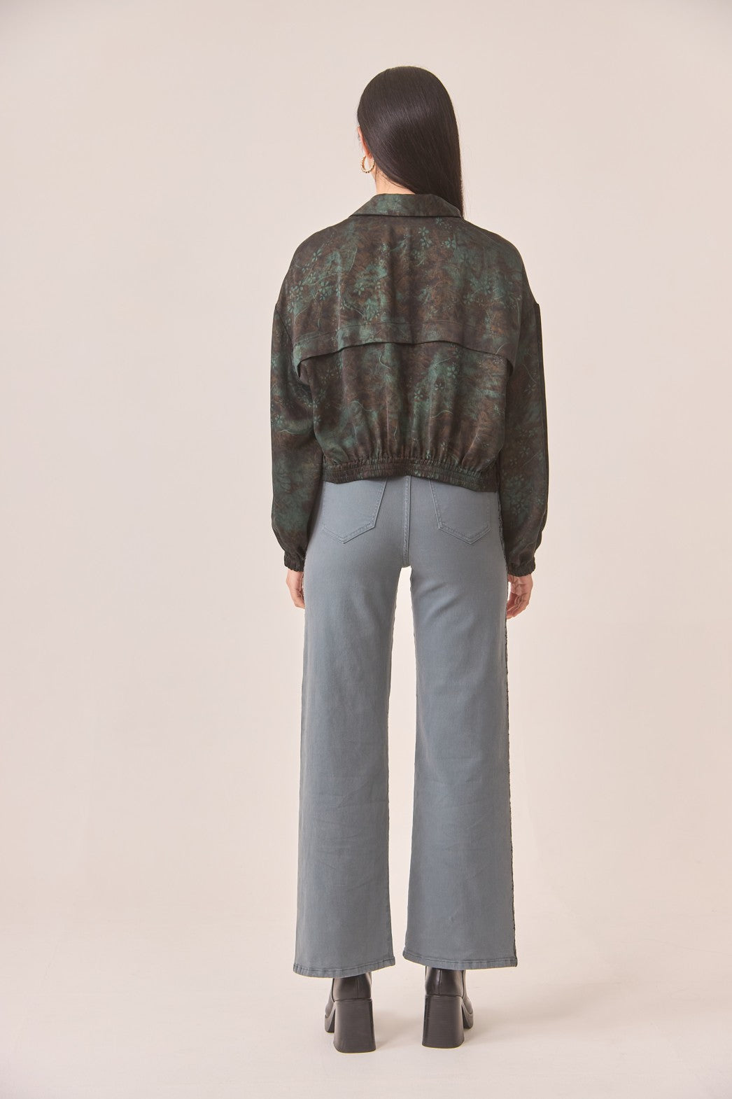 Person wearing a green and brown patterned jacket and light gray pants on a beige background