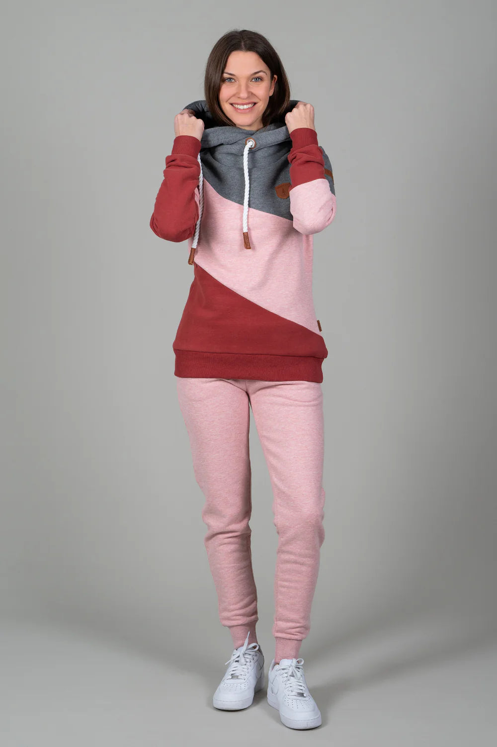 Woman wearing a two-tone hoodie and pink pants on a gray background
