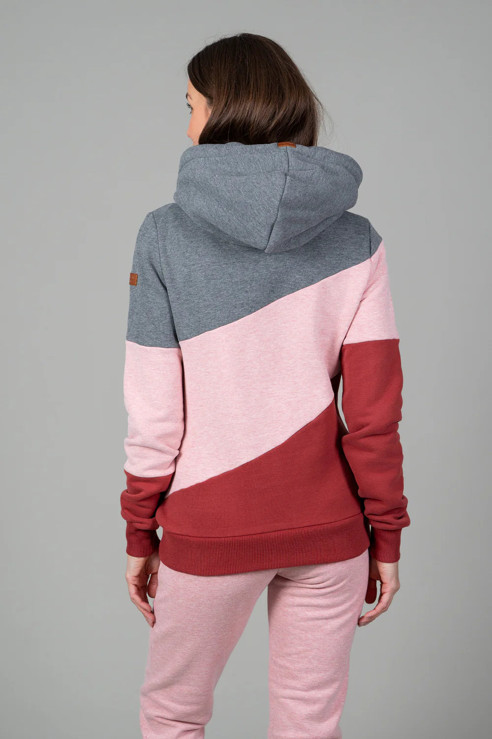 Person wearing a color-blocked hoodie with gray, pink, and red sections on a gray background
