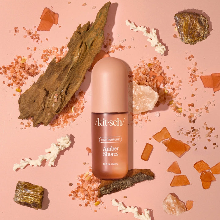 Kitsch Amber Shores hair perfume bottle on a pink background with natural elements.