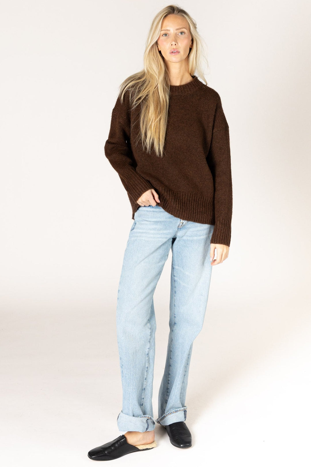 Woman wearing a brown sweater and light blue jeans on a white background