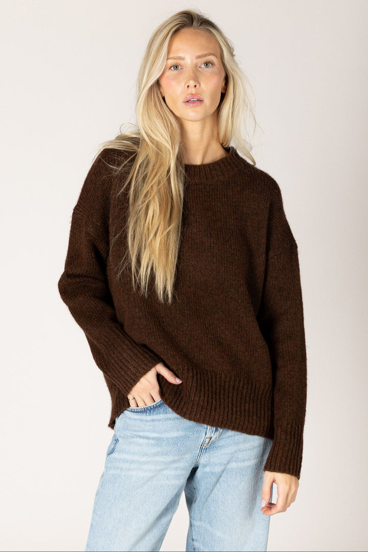 Woman wearing a brown sweater and light blue jeans against a plain background