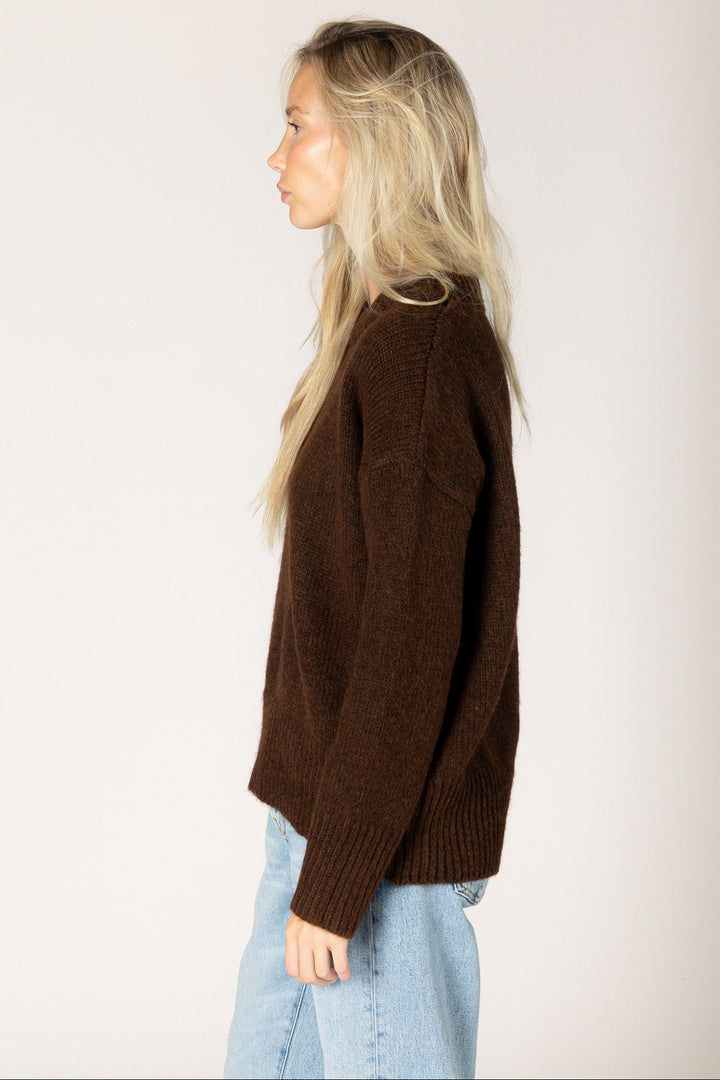 Woman wearing a brown sweater and light blue jeans against a plain background