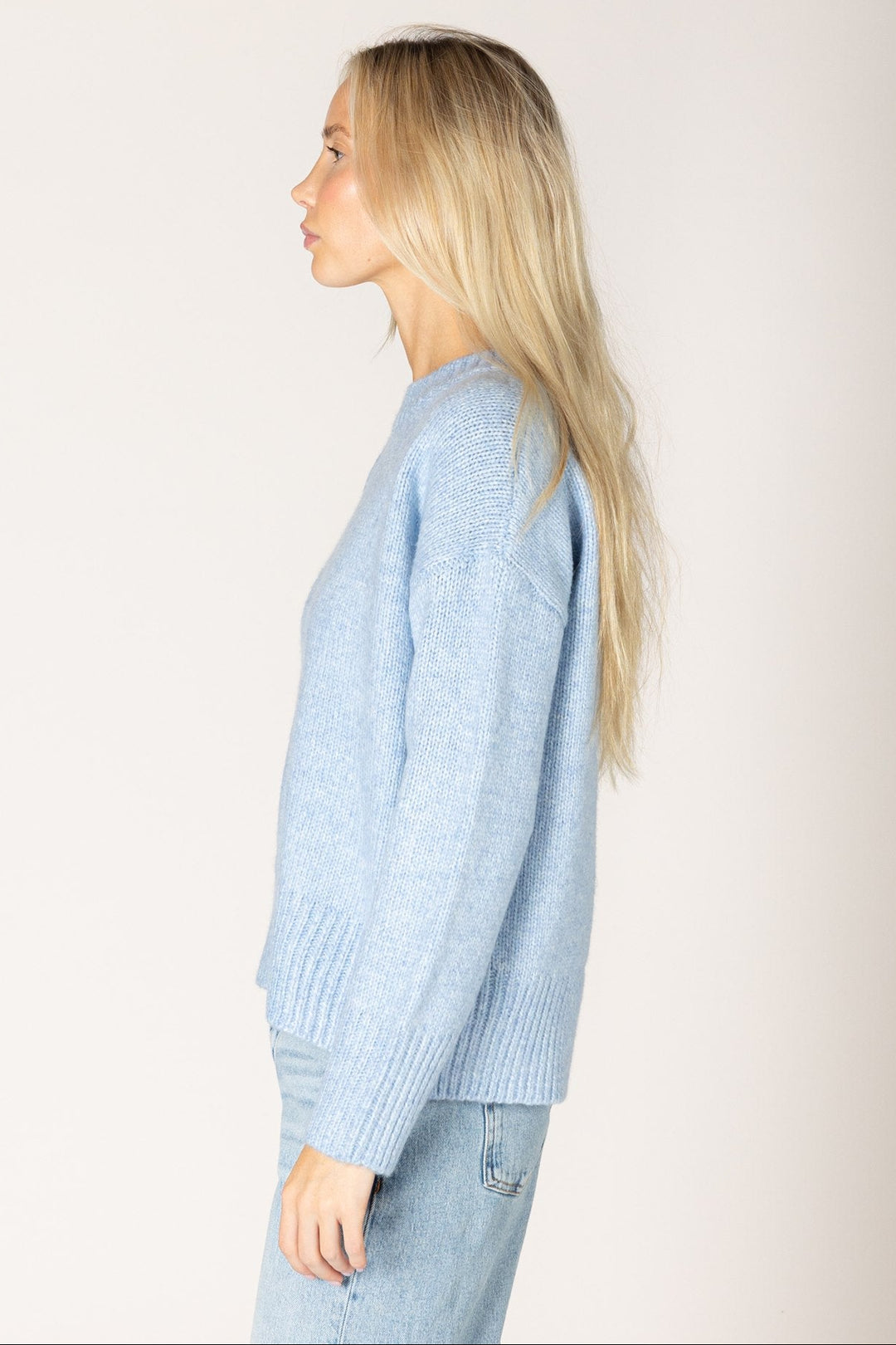Woman wearing a light blue sweater and jeans against a plain background