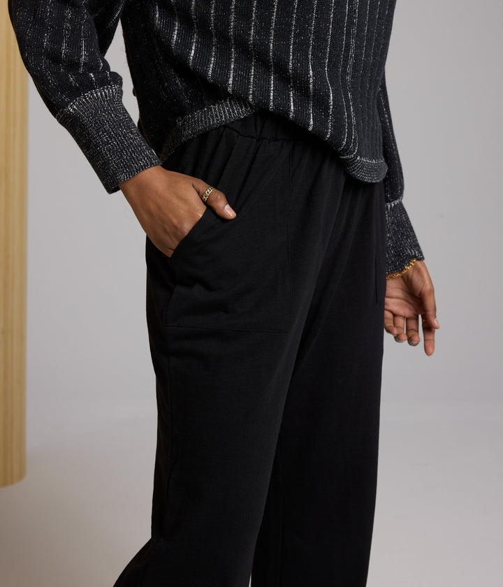 Person wearing a dark pinstripe sweater and black pants against a neutral background