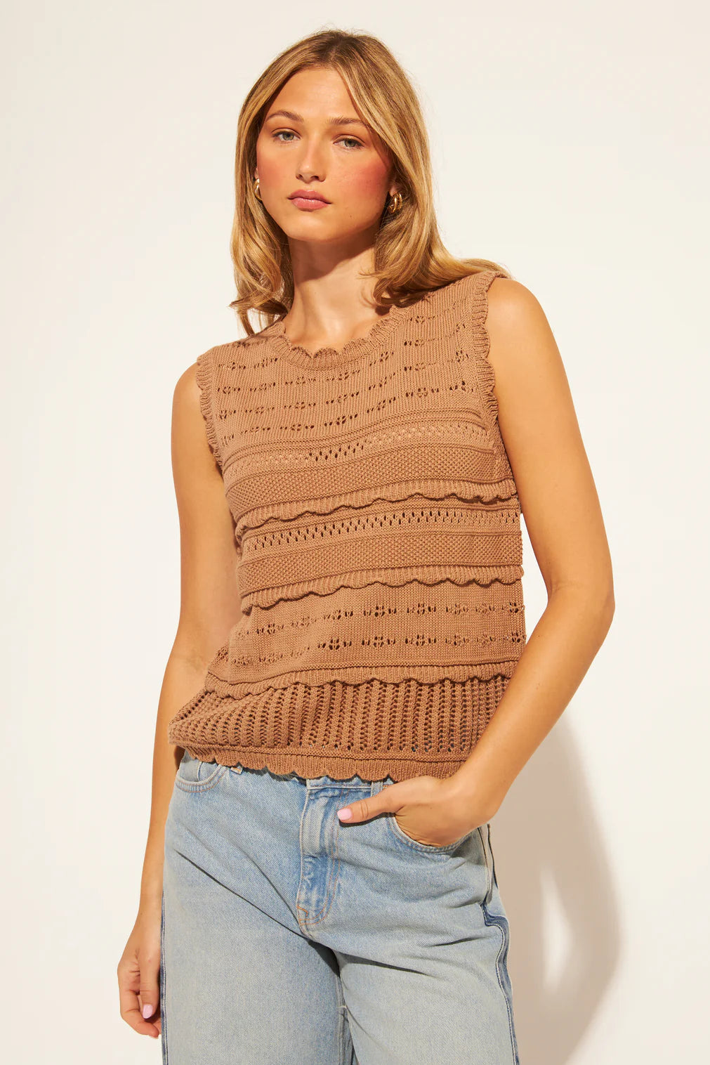 Woman wearing a brown sleeveless knitted top against a plain background