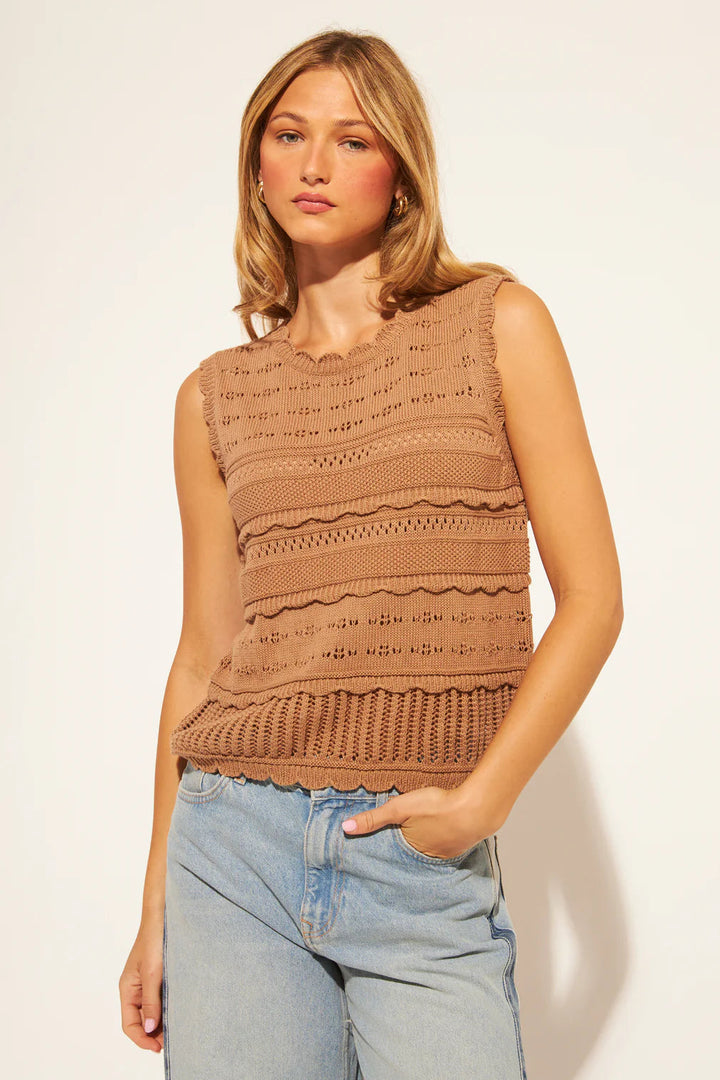 Woman wearing a brown sleeveless knitted top against a plain background