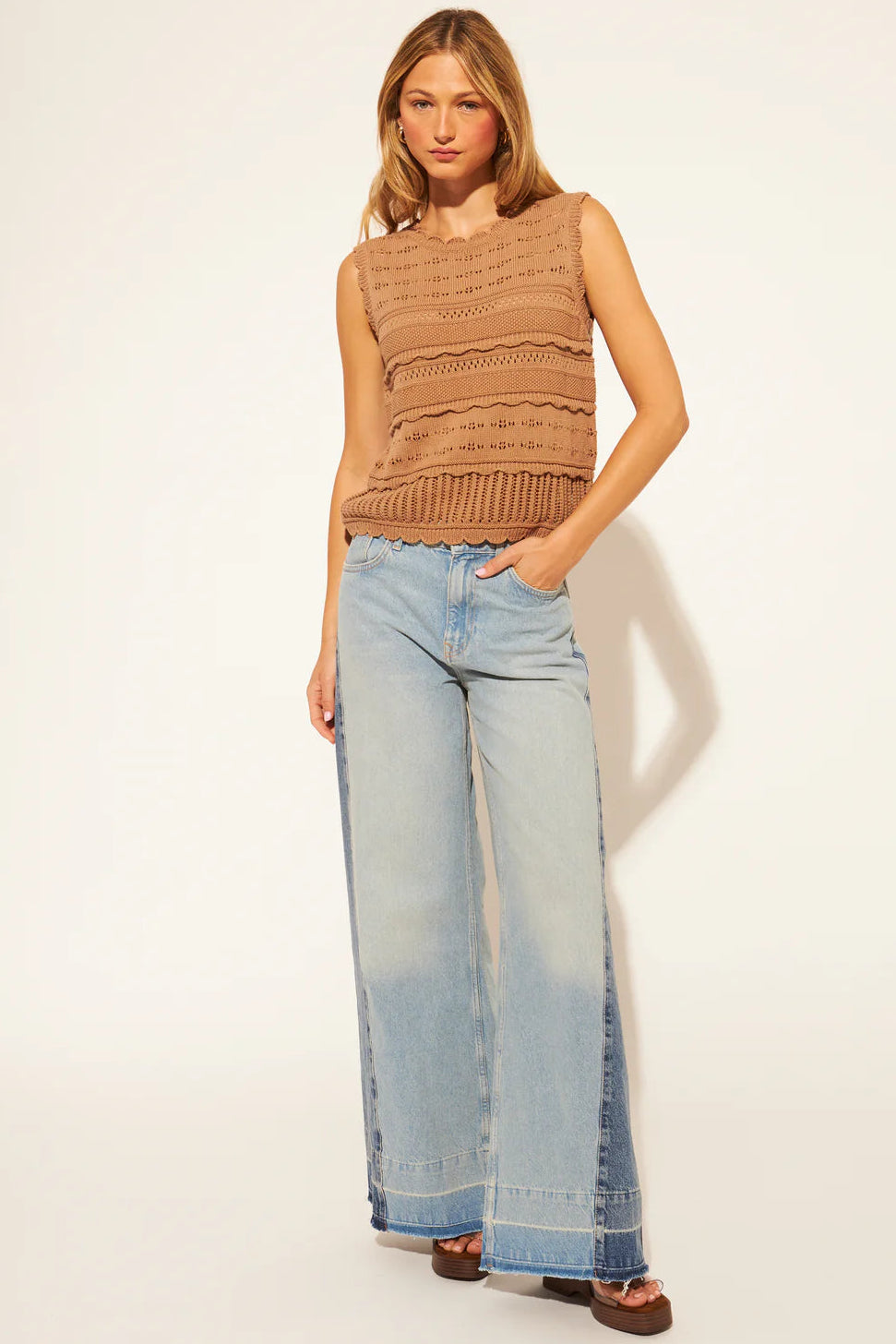 Woman wearing a brown sleeveless top and light blue jeans on a white background