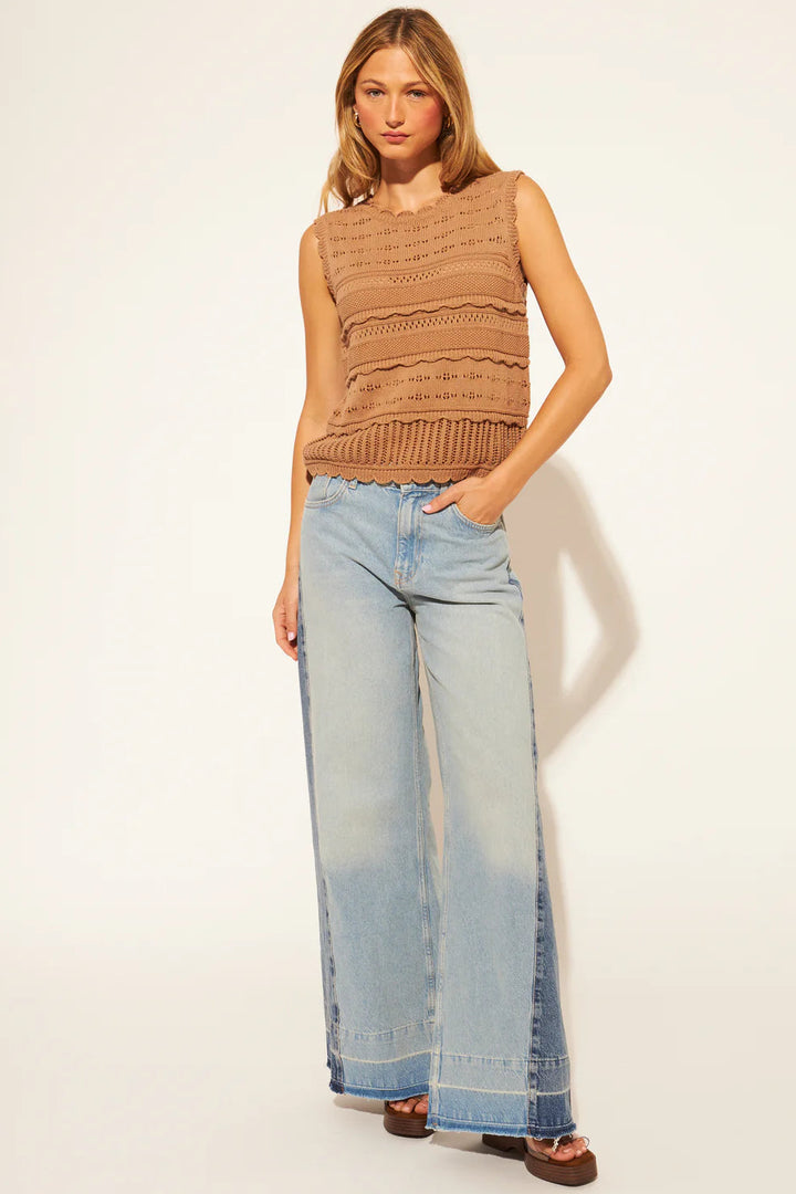 Woman wearing a brown sleeveless top and light blue jeans on a white background