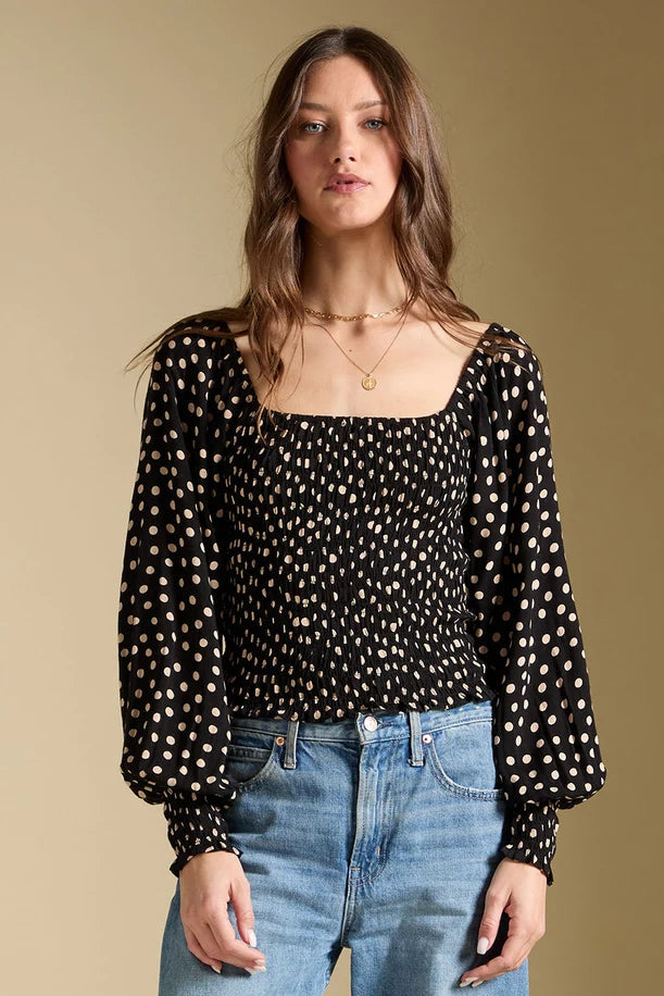 Woman wearing a black polka dot blouse and blue jeans against a beige background