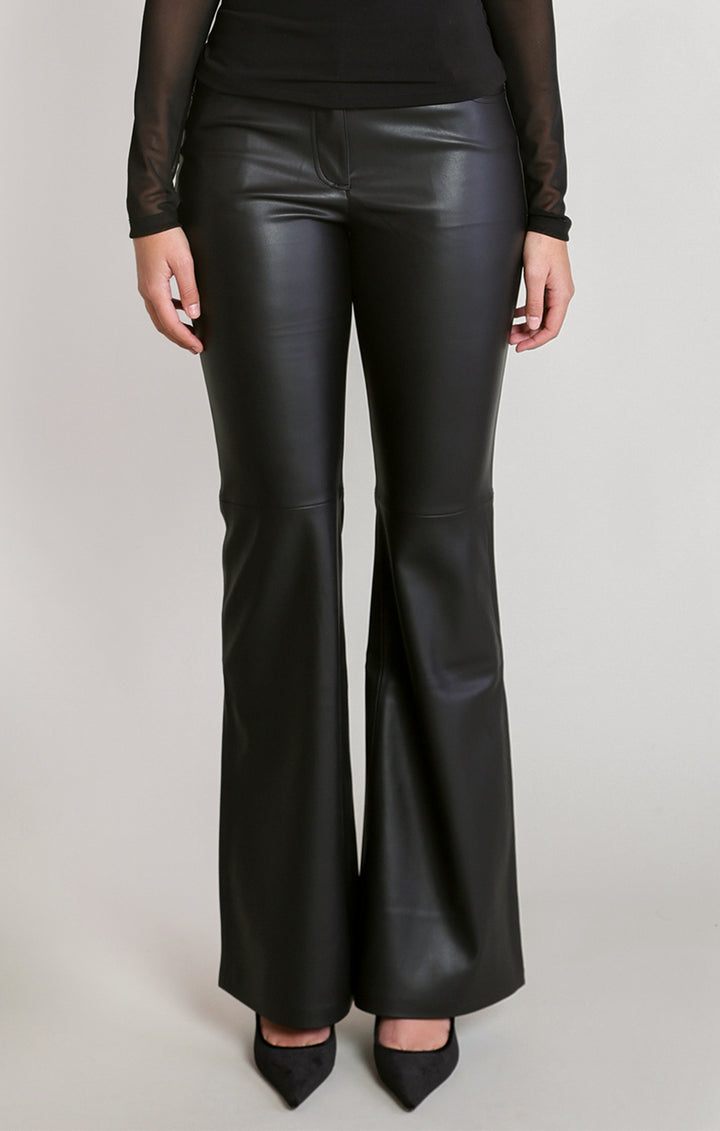 Black faux-leather flare pants worn by a model, paired with a black sheer long-sleeve top and black pointed-toe heels, against a light gray studio background.